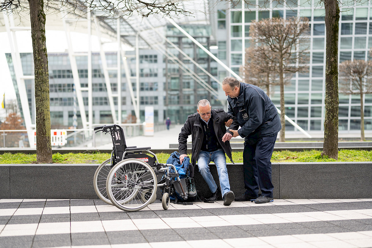 Ein Service Agent hilft einem Mann mit eingeschränkter Mobilität in den Rollstuhl.