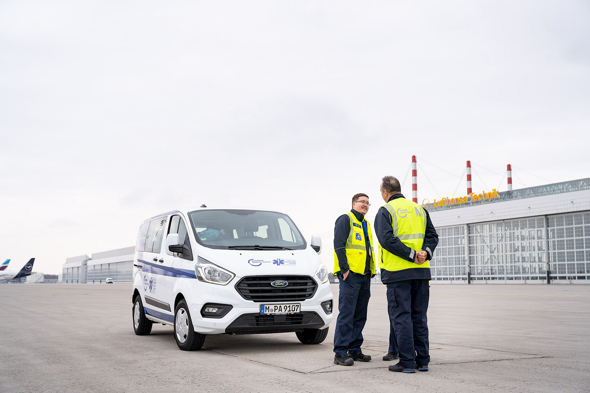 Zwei Service Agents unterhalten sich vor einem Mobility Service Transporter auf dem Vorfeld des Münchner Flughafens.