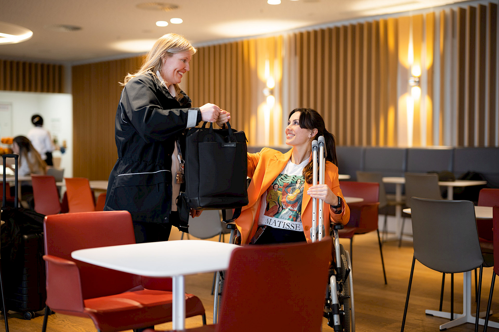 Service Agent nimmt junger Frau im Rollstuhl eine schwere Tasche ab.