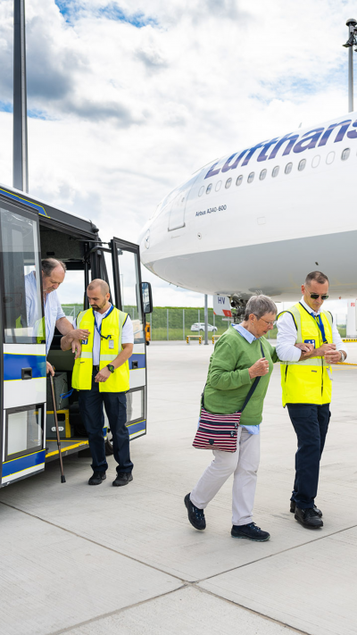 Zwei Service Agents helfen einer Frau und einem Mann mit eingeschränkter Mobilität auf dem Weg zum Flugzeug.