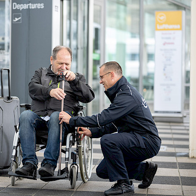 Service Agent hilft älterem Mann mit Reisegepäck und Rollstuhl.