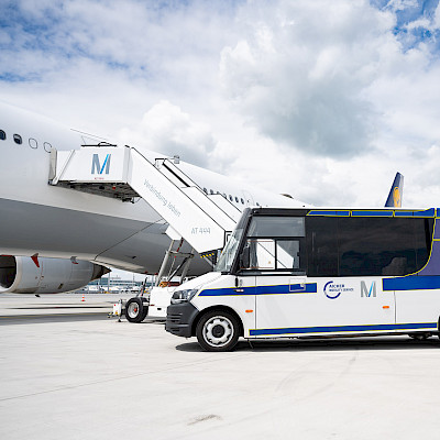 Ein Minibus des Mobility Service steht vor einem Flugzeug auf dem Vorfeld des Flughafen München.