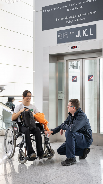 Ein Service Agent spricht mit einer jungen Frau im Rollstuhl.