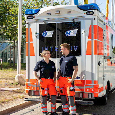 Rettungssanitäter und Rettungssanitäterin unterhalten vor dem Einsatzfahrzeug.