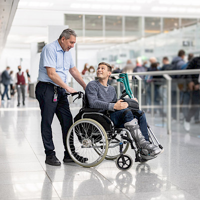 Ein Service Agent spricht mit einem jungen Mann mit Beinschiene im Rollstuhl.