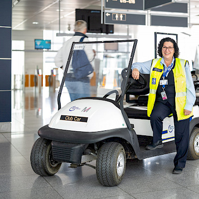 Weiblicher Service Agent steht neben einem E-Car und lächelt in die Kamera.