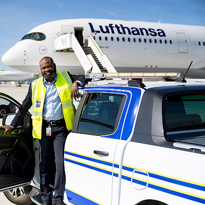Männlicher Service Agent steht neben einem Pick-up des Mobility Service auf dem Vorfeld des Flughafen München.
