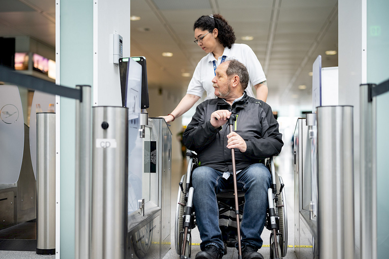 Eine Servicemitarbeiterin des Mobility Service hilft einem älteren Mann bei der Sicherheitskontrolle am Flughafen.